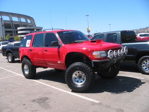 1986 Ford Bronco - Modified red SUV with large tires and auxiliary lights parked in a lot.