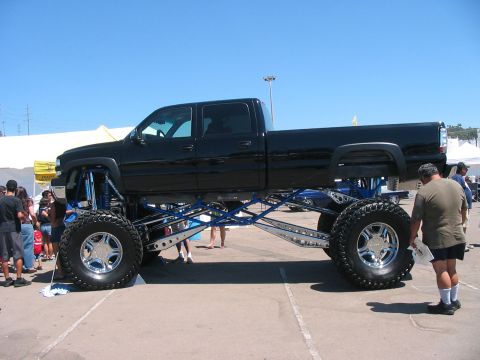 1986 Ford Bronco - A heavily modified black pickup truck with an extreme lift kit and custom suspension is displayed at an outdoor event.