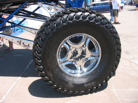 1986 Ford Bronco - Custom lifted truck's large tire and suspension components are shown, with another vehicle in the background.