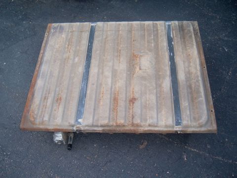 1971 Ford Ranchero - A metal fuel tank with a ribbed surface and two dark straps is shown resting on the ground.