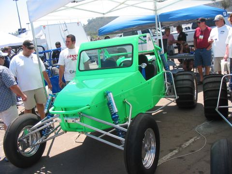 1986 Ford Bronco - A custom-built dune buggy is displayed outdoors under a tent, with several onlookers present.