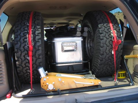 1986 Ford Bronco - The cargo area of an SUV is shown with two spare tires, a toolbox, and a jack, suggesting preparation for off-road adventures.