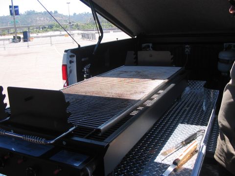 1986 Ford Bronco - A pickup truck bed is outfitted with a large grill and a propane tank, ready for outdoor cooking.