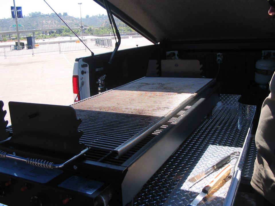Pickup truck bed loaded with a large grill and propane tank