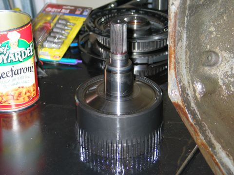 1995 Ford Bronco - A transmission torque converter and its associated parts are laid out on a workbench, alongside a can of Chef Boyardee Beefaroni and a set…