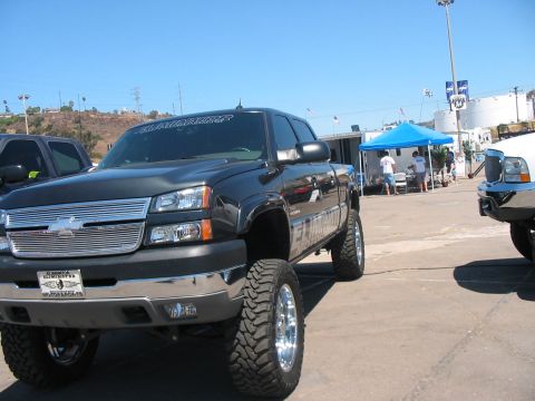 1986 Ford Bronco - A lifted pickup truck is parked at an outdoor event with other vehicles and tents visible.