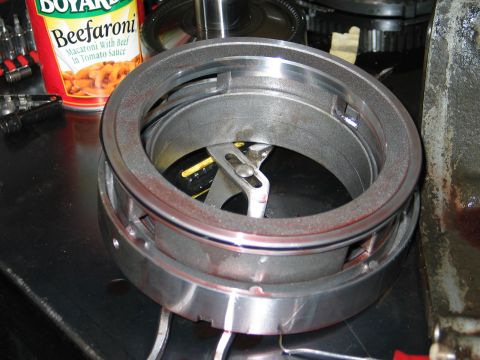 1995 Ford Bronco - A metal transmission part sits on a workbench next to a can of Beefaroni, with visible red fluid residue.