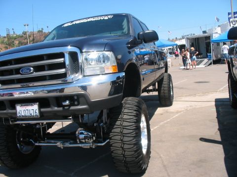 1986 Ford Bronco - A lifted dark blue Ford F-250 truck is displayed at an outdoor event, a prominent chrome grille and oversized tires.