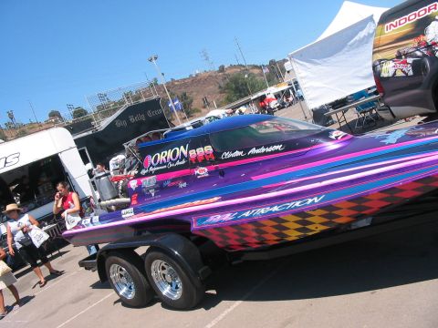 1986 Ford Bronco - A custom-painted race boat named "REAL ATTRACTION" is displayed on a trailer at an outdoor event.