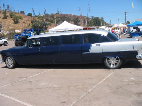 1986 Ford Bronco - A custom-built limousine, likely a 1955 Chevrolet, sits in a parking lot with other vehicles and tents in the background.