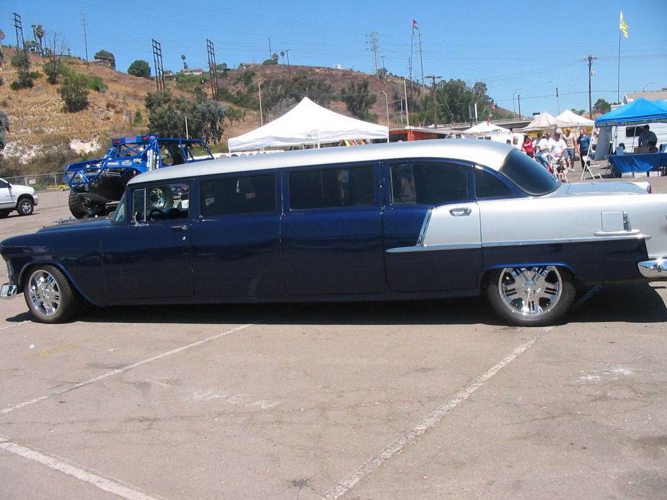 Two-tone blue and silver stretched sedan with chrome wheels. A blue off-road vehicle is parked behind it