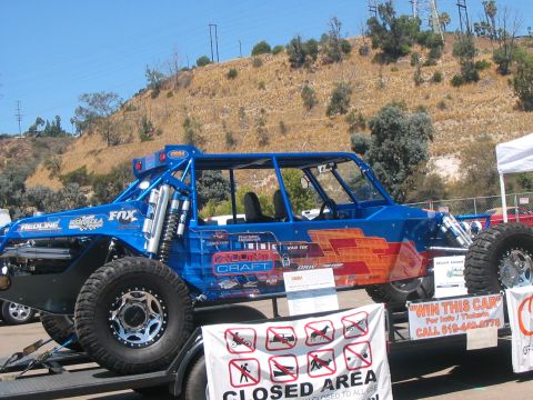 1986 Ford Bronco - A custom-built off-road buggy is displayed on a trailer, adorned with numerous sponsor logos and graphics.