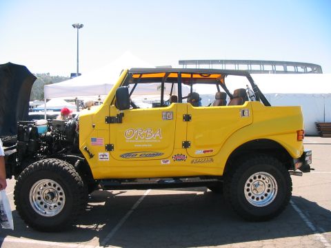 1986 Ford Bronco - A yellow off-road vehicle with an exposed engine is parked outdoors, possibly at a car show.