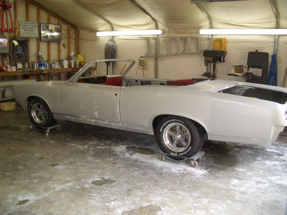 Side view of a 1967 Pontiac GTO convertible in primer, on dollies in a garage