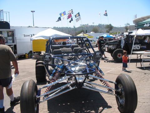 1986 Ford Bronco - A custom dune buggy is displayed at a car show, with other vehicles and tents in the background.