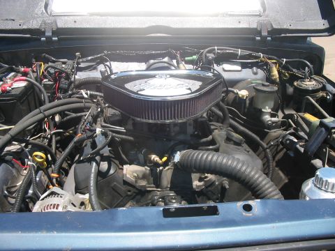 1986 Ford Bronco - The engine bay of a blue vehicle is shown, a prominent chrome air filter assembly.