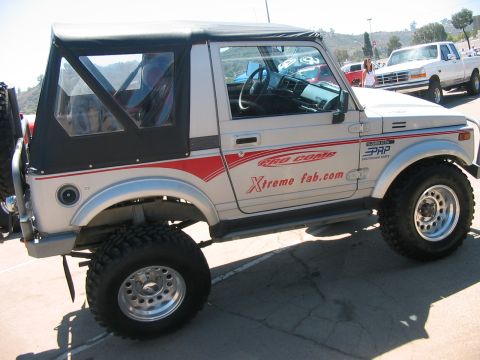 1986 Ford Bronco - Side view of a modified Suzuki Samurai with custom graphics, parked outdoors with another vehicle behind it.