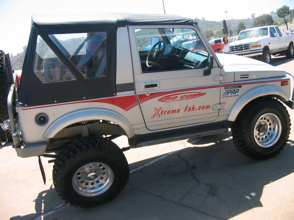 Suzuki Samurai with 'Rad Comp' and 'Xtreme fab.com' decals on the side. White pickup truck in background