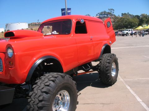 1986 Ford Bronco - A bright red custom van with a lifted suspension and oversized tires sits parked outdoors.
