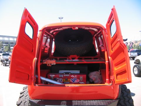 1986 Ford Bronco - This orange van, possibly a custom build, displays its interior storage with a spare tire and a toolbox adorned with various stickers.