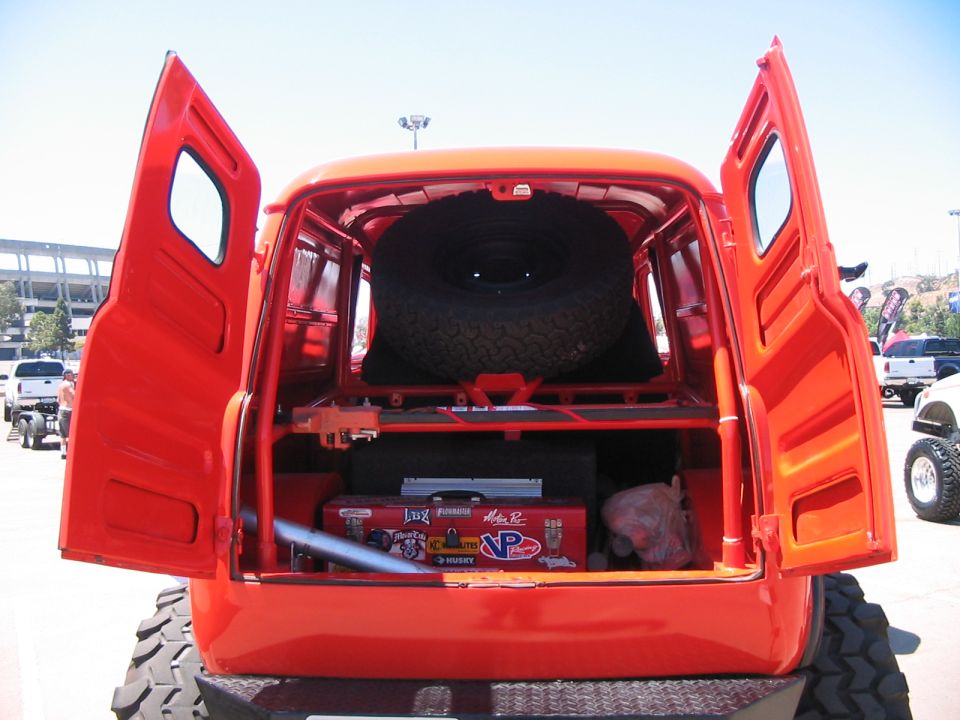 Orange van's open rear doors reveal spare tire and toolbox with stickers