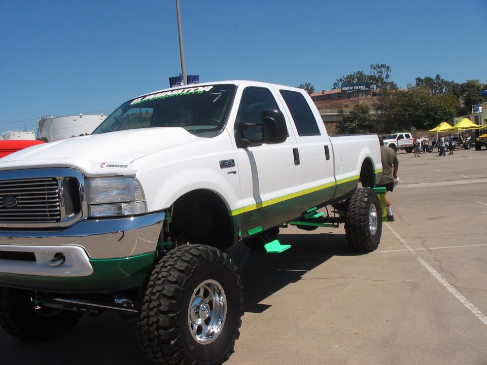 White lifted pickup truck with green and yellow accents, large off-road tires, and custom hood