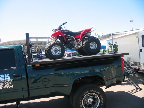 1986 Ford Bronco - A red ATV is loaded onto the bed of a green pickup truck, with visible text on the truck's door.