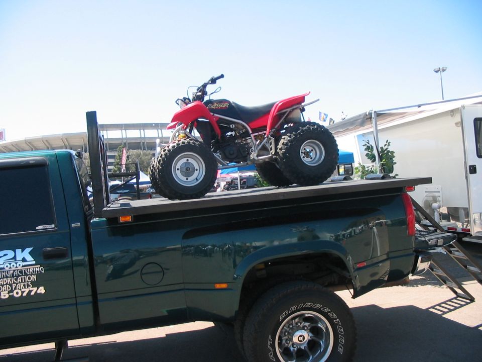 Red ATV on a green pickup truck bed with text '2K MANUFACTURING FABRICATION ROAD PARTS 5-0774' on the truck