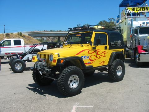 1986 Ford Bronco - A bright yellow Jeep Wrangler with custom flame decals is parked at an outdoor event.