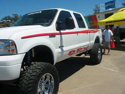 1986 Ford Bronco - A lifted white pickup truck is parked outside under a yellow tent with people in the background.