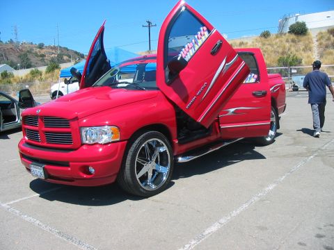 1986 Ford Bronco - This red pickup truck features custom lambo doors and chrome rims, with other vehicles visible in the background.