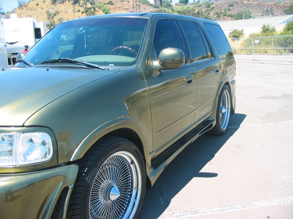 Green SUV with custom side skirts and wire wheels, front quarter view