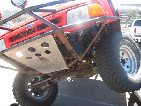 1986 Ford Bronco - A modified red Ford truck is shown from the front, lifted with off-road tires and a custom bumper.