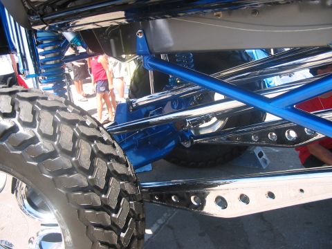 1986 Ford Bronco - A highly customized suspension system with bright blue components and polished metal is visible, along with a large off-road tire.