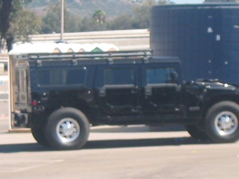 1986 Ford Bronco - A black Hummer H1 with a roof rack is parked outdoors next to a large blue cylindrical object.