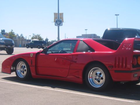 1986 Ford Bronco - A red Ferrari F40 is parked in a lot, with other vehicles visible in the background.