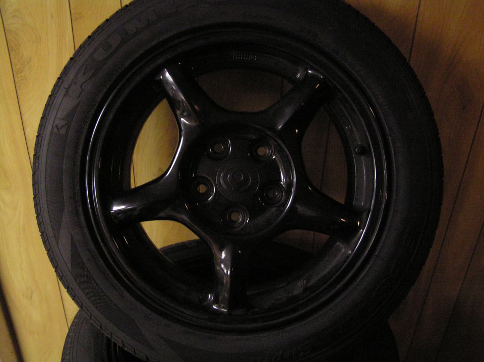 Black five-spoke alloy wheel with Kumho tire leaning against a wood-paneled wall