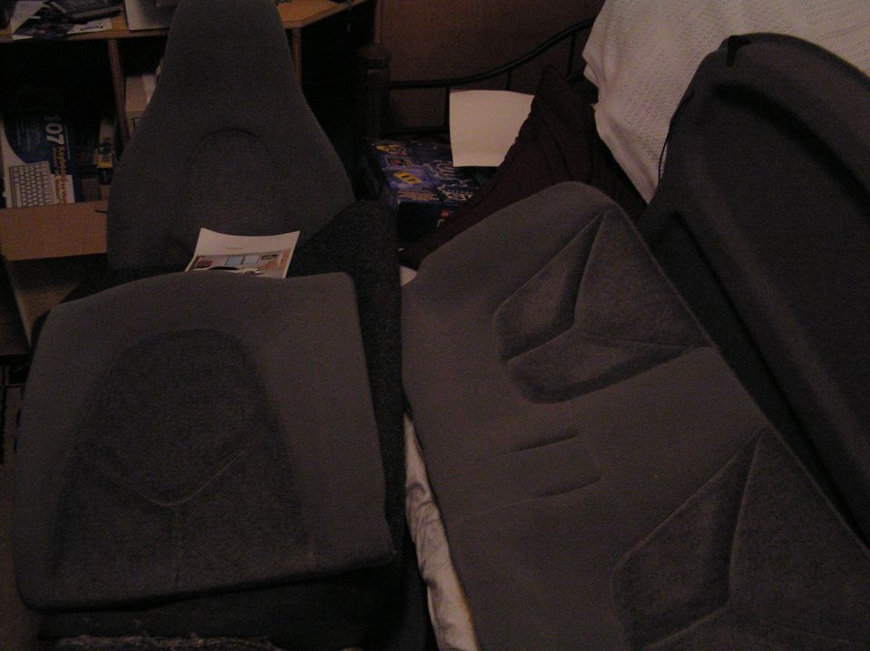 Dark gray cloth car seats removed and stacked in a cluttered bedroom