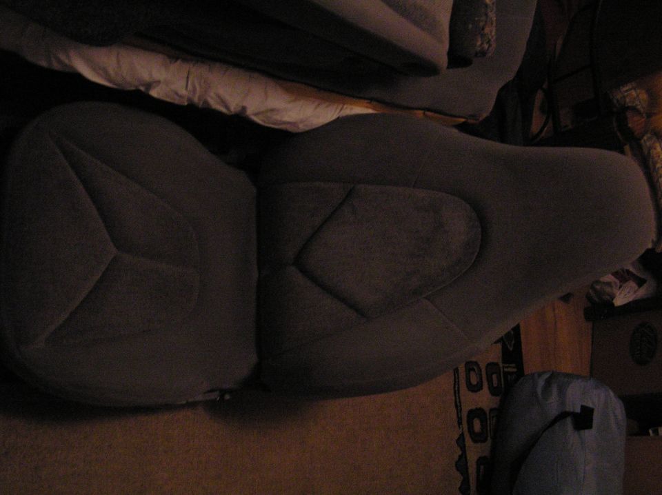Gray cloth bucket seats laid out on a bed in a dim room