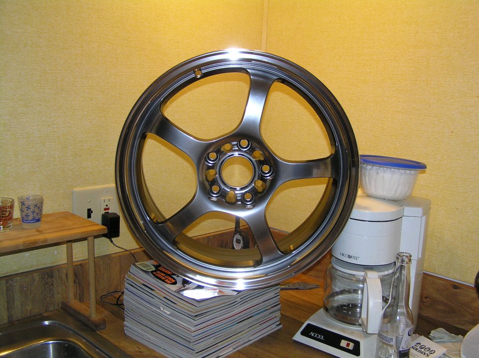 Front face of a polished gunmetal five-spoke alloy wheel on a wood counter