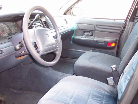 2000 Ford Crown Victoria - The interior of a car is shown, the driver's side dashboard, steering wheel, and front seats. The model year is not discernible from the im…