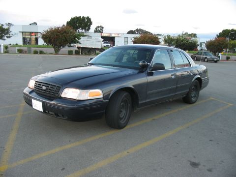2000 Ford Crown Victoria - A dark blue 2000 Ford Crown Victoria is parked in a lot with a truck and another car in the background.