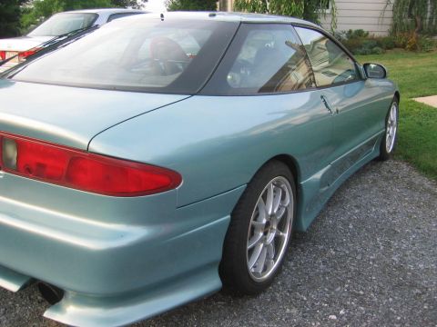1993 Ford Probe - The rear quarter panel and taillight of a teal 1993 Ford Probe are visible, parked on a gravel driveway.