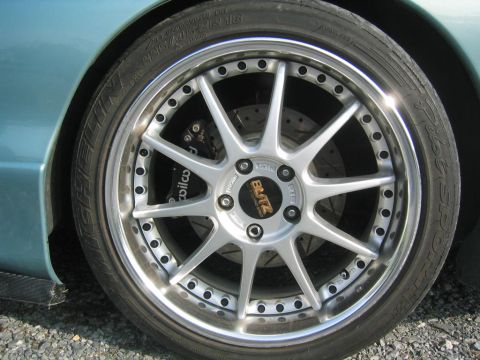 1993 Ford Probe - Close-up of a multi-spoke silver aftermarket wheel with polished lip and exposed rim bolts, mounted on a light blue-green car. The tire is…