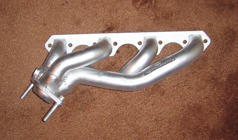 1986 Ford Bronco - A silver exhaust manifold is shown against a brown background, with visible text on one of the pipes.