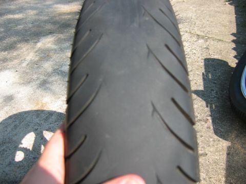 1985 Ford Crown Victoria LTD - A motorcycle tire is held up for inspection on a concrete surface.