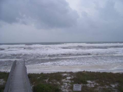 1995 Ford Bronco - Wooden walkway leads to a beach with rough waves under a cloudy sky.