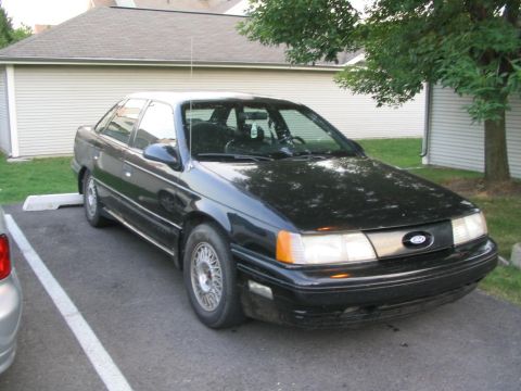 1990 Ford Taurus - A black 1990 Ford Taurus is parked outside a building with trees nearby.
