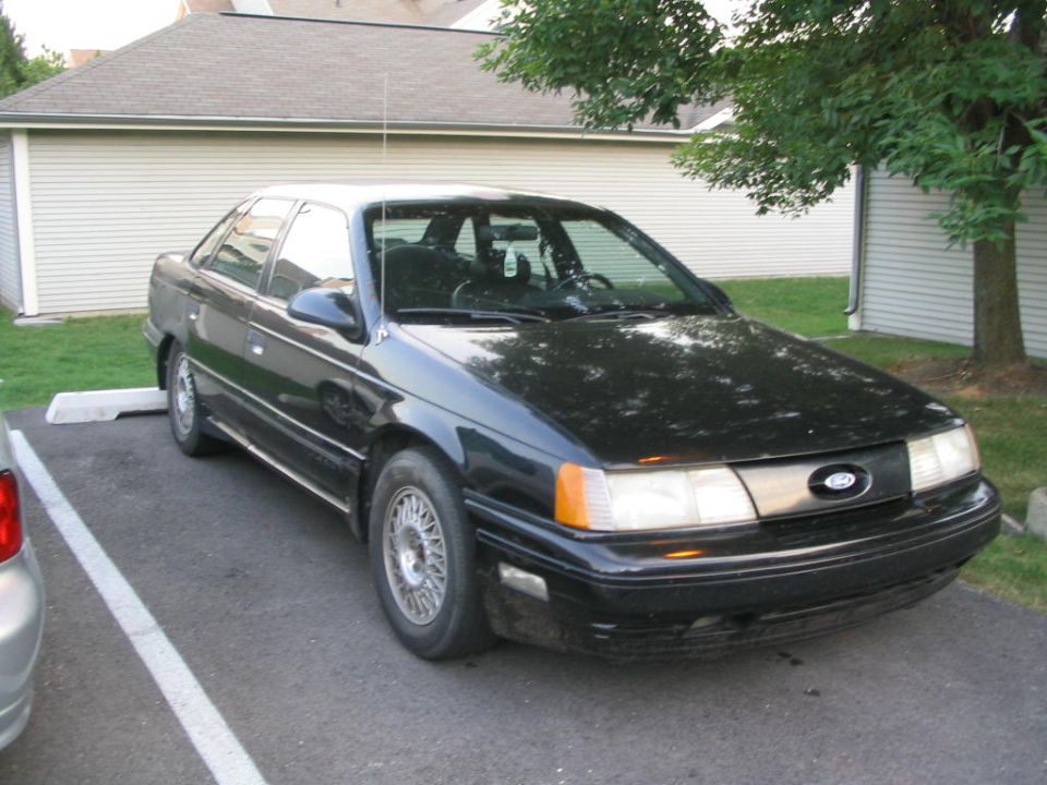 Black 1990 Ford Taurus parked in a lot. Front end is visible