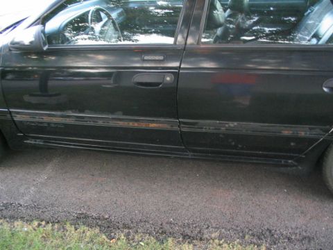 1990 Ford Taurus - The side of a black sedan shows wear and tear along the lower body panels and trim.